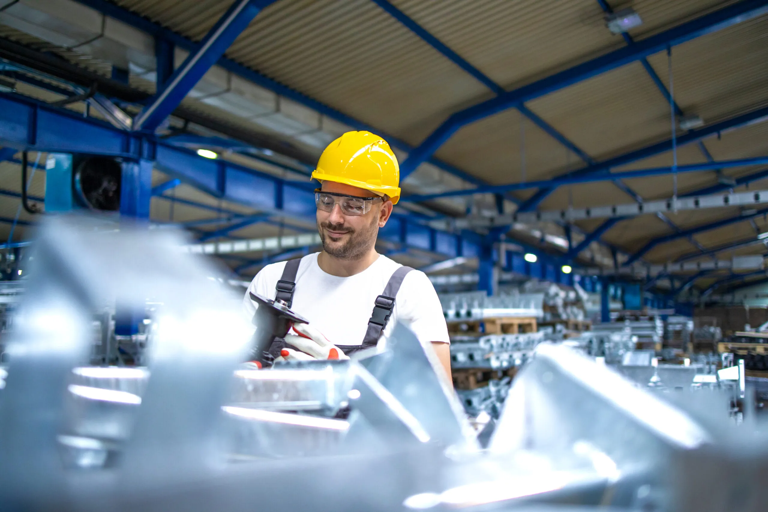 Worker in a hard hat and safety glasses at a machine in a production hall