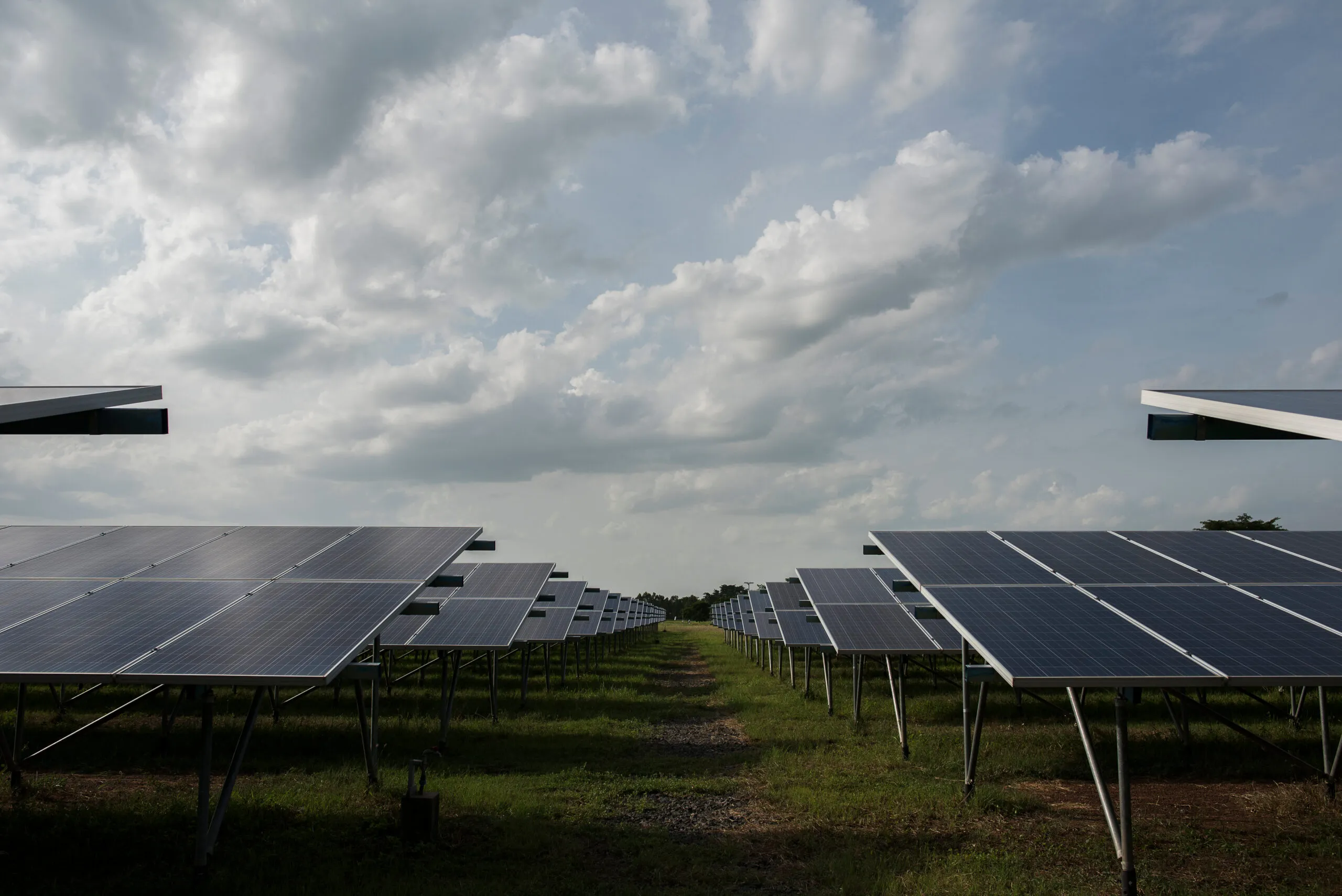 Rows of solar panels in a field under a clouded sky